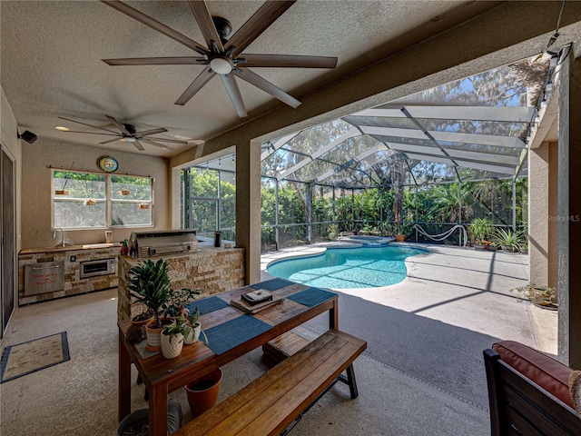 view of swimming pool with a patio, glass enclosure, area for grilling, a pool with connected hot tub, and exterior kitchen