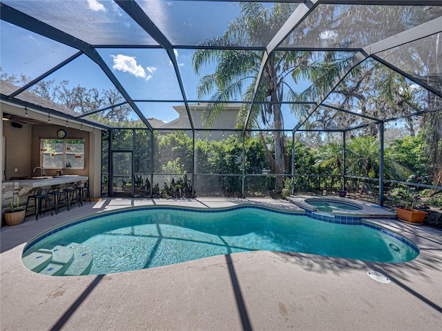 view of pool with a patio area, a pool with connected hot tub, glass enclosure, and outdoor dry bar