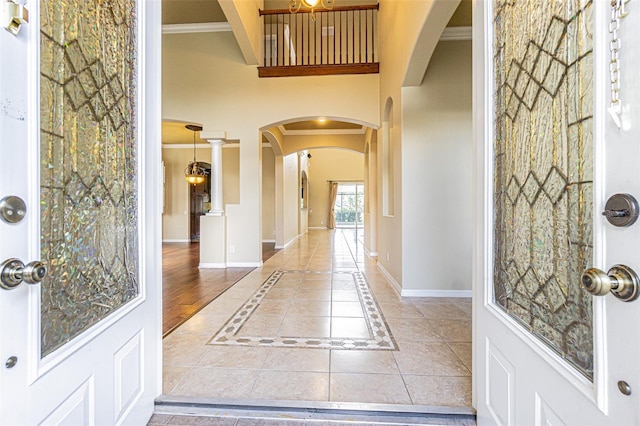 foyer with arched walkways, crown molding, tile patterned flooring, and baseboards