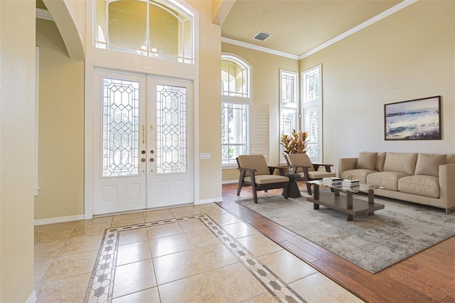 foyer featuring crown molding, a towering ceiling, visible vents, and baseboards