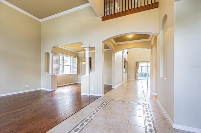 interior space featuring arched walkways, crown molding, decorative columns, a towering ceiling, and baseboards