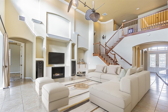 living area with arched walkways, a lit fireplace, french doors, and crown molding