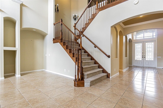 tiled entrance foyer featuring arched walkways, a towering ceiling, baseboards, french doors, and crown molding