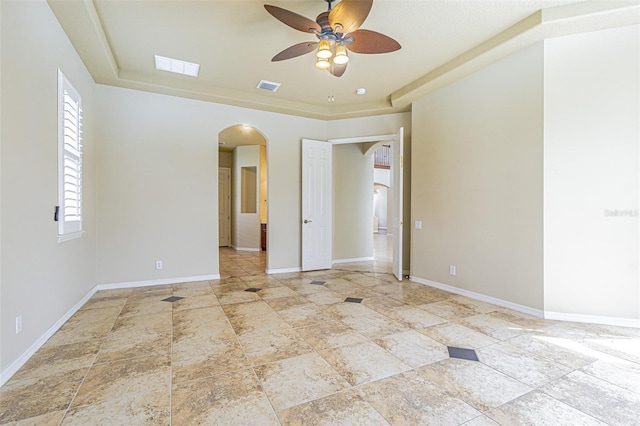 unfurnished room featuring arched walkways, a raised ceiling, visible vents, and baseboards