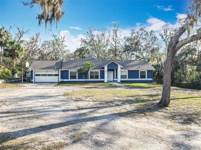 ranch-style home featuring a garage, a front lawn, and gravel driveway