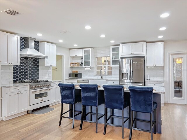 kitchen featuring light wood finished floors, visible vents, a kitchen island, stainless steel appliances, and wall chimney range hood