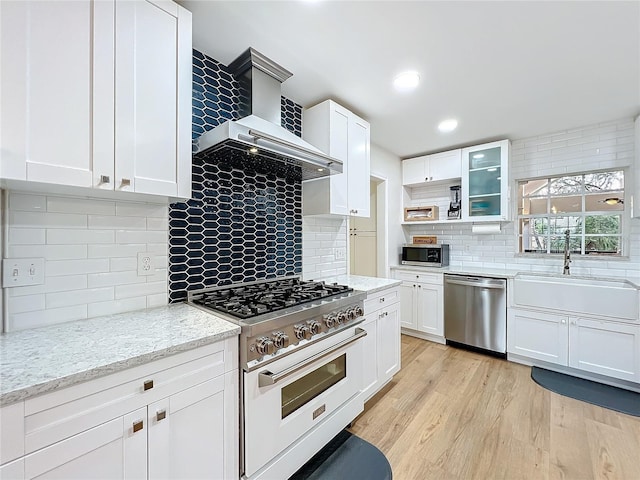 kitchen featuring a sink, white cabinets, light wood-style floors, appliances with stainless steel finishes, and wall chimney exhaust hood