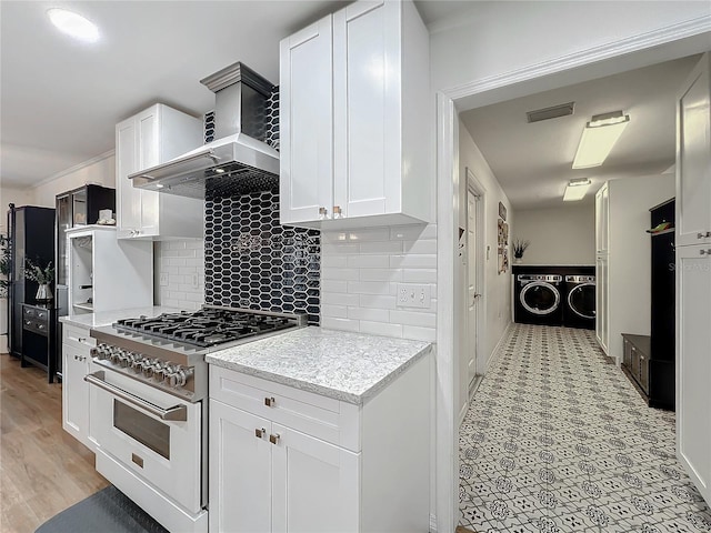 kitchen featuring white cabinets, washer and dryer, range with gas stovetop, wall chimney range hood, and backsplash