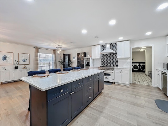 kitchen with stainless steel appliances, separate washer and dryer, a kitchen island, white cabinets, and wall chimney range hood