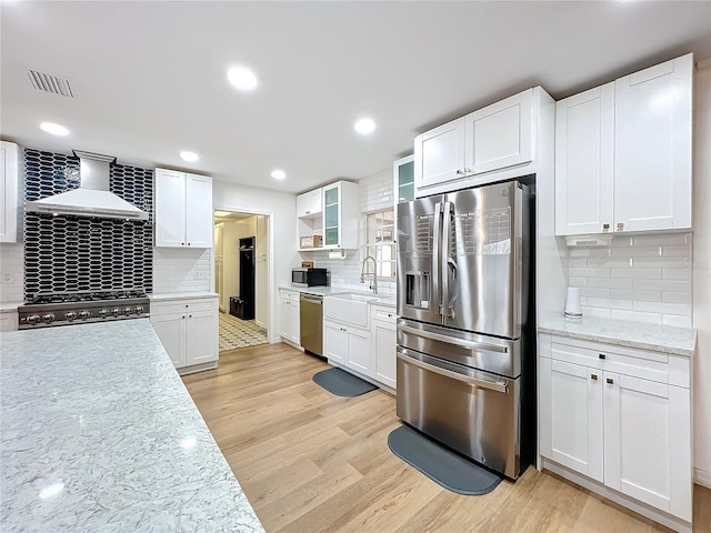 kitchen featuring wall chimney exhaust hood, appliances with stainless steel finishes, white cabinets, and light wood-style floors