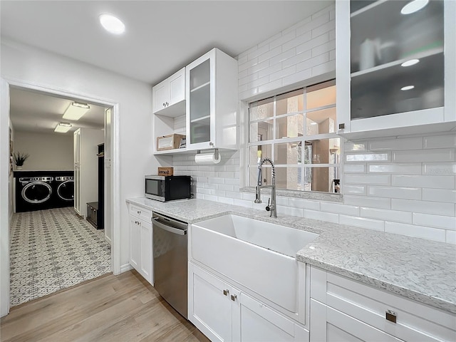 kitchen with stainless steel appliances, a sink, white cabinets, tasteful backsplash, and washer and clothes dryer