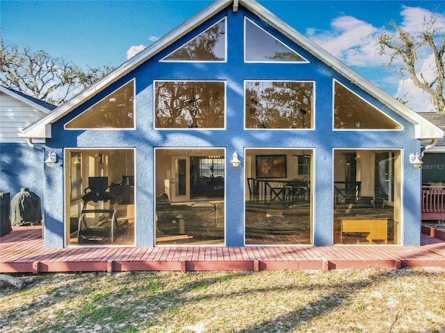 back of property featuring a sunroom, a wooden deck, and stucco siding