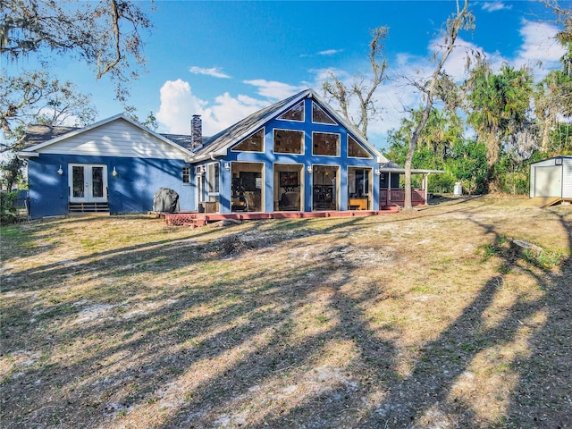 back of house featuring a yard, a chimney, an outdoor structure, and french doors