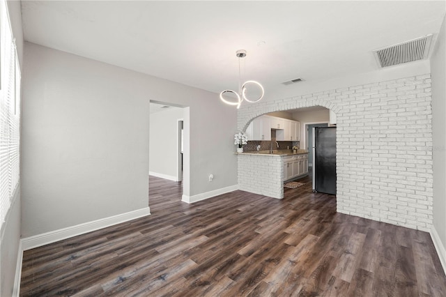 interior space with dark wood-style floors, brick wall, visible vents, and baseboards