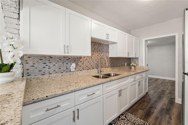 kitchen featuring a sink, white cabinets, backsplash, light stone countertops, and dark wood finished floors