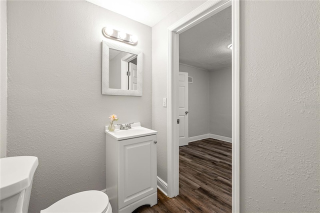 half bath with baseboards, a textured wall, toilet, wood finished floors, and vanity