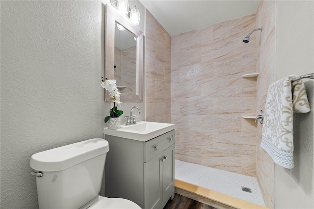 bathroom featuring tiled shower, a textured wall, vanity, and toilet