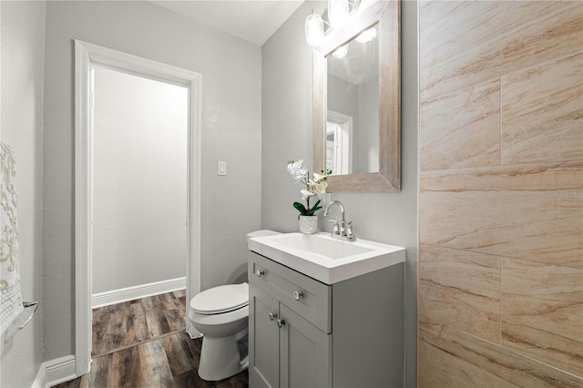 half bathroom with baseboards, vanity, toilet, and wood finished floors