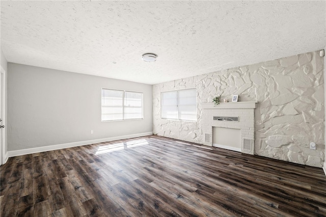 unfurnished living room featuring baseboards, visible vents, wood finished floors, a textured ceiling, and a fireplace