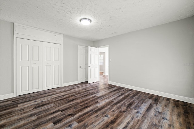 unfurnished bedroom with a textured ceiling, dark wood-style flooring, a closet, and baseboards