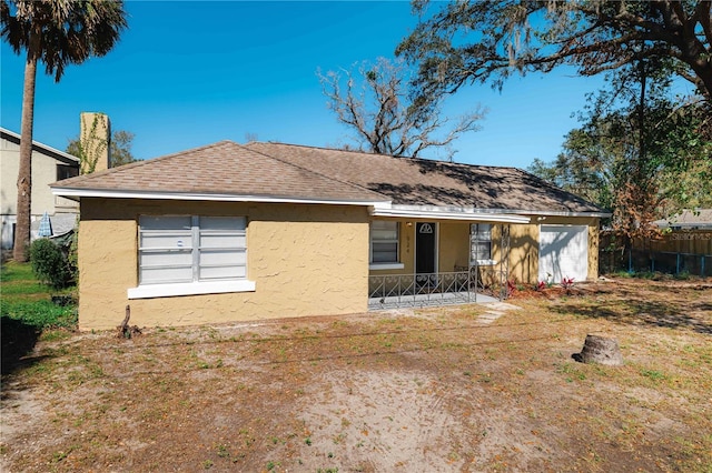 rear view of house with a porch, roof with shingles, fence, and stucco siding