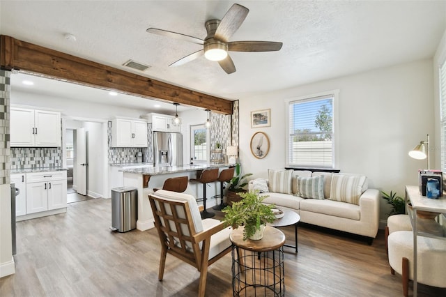 living area with beam ceiling, visible vents, light wood-style flooring, and a textured ceiling