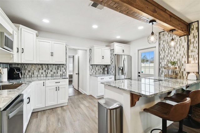 kitchen with light wood finished floors, visible vents, appliances with stainless steel finishes, a breakfast bar, and white cabinetry