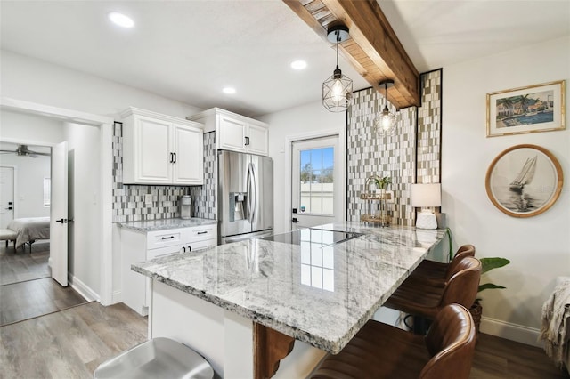 kitchen with stainless steel fridge, tasteful backsplash, white cabinets, a breakfast bar area, and wood finished floors