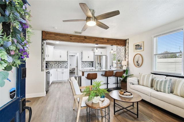 living room featuring ceiling fan, light wood finished floors, beamed ceiling, and visible vents