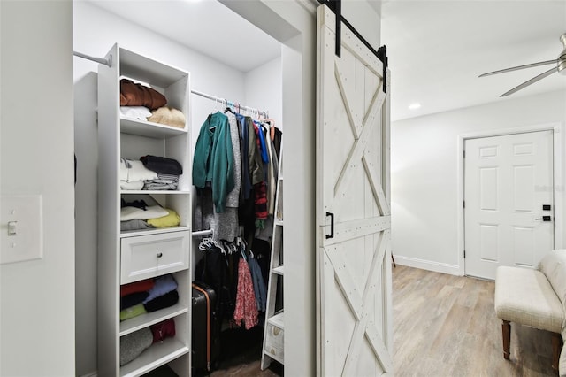 spacious closet featuring a barn door, wood finished floors, and a ceiling fan