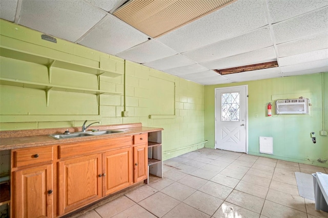 kitchen with concrete block wall, brown cabinetry, an AC wall unit, open shelves, and a sink