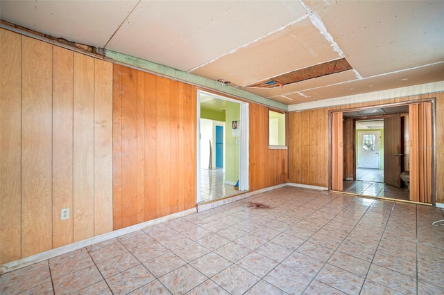 tiled spare room featuring wood walls and baseboards