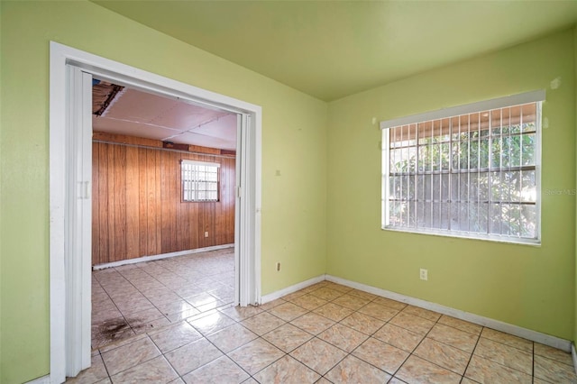 empty room featuring baseboards, tile patterned flooring, a wealth of natural light, and wooden walls