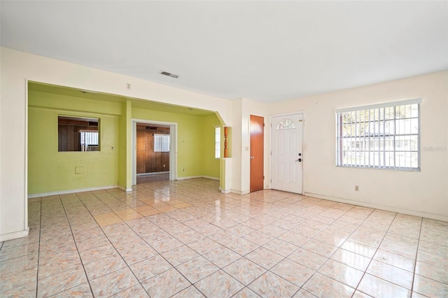 unfurnished room featuring arched walkways, light tile patterned flooring, visible vents, and baseboards