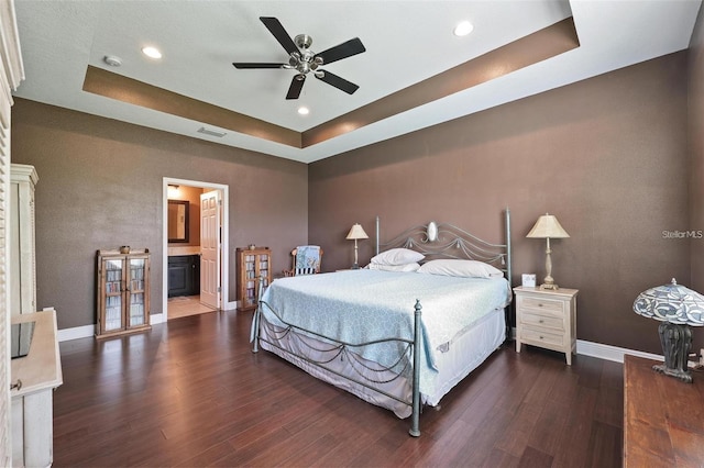 bedroom with a tray ceiling, wood finished floors, visible vents, and baseboards