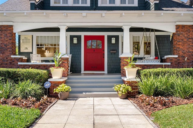 view of exterior entry featuring covered porch and roof with shingles