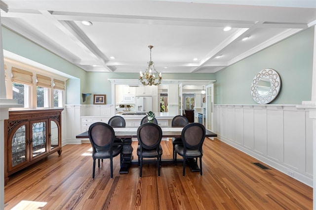 dining area featuring coffered ceiling, beam ceiling, light wood-style floors, wainscoting, and a notable chandelier