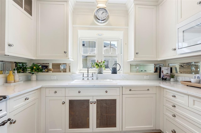 kitchen featuring white microwave, white cabinetry, light stone counters, and a sink