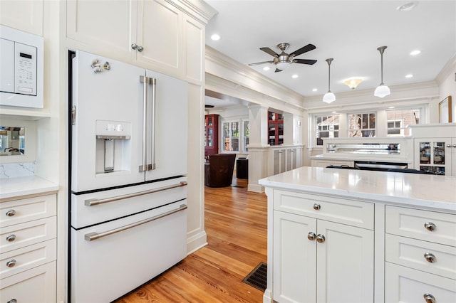 kitchen featuring light stone countertops, light wood-type flooring, ornamental molding, hanging light fixtures, and white appliances