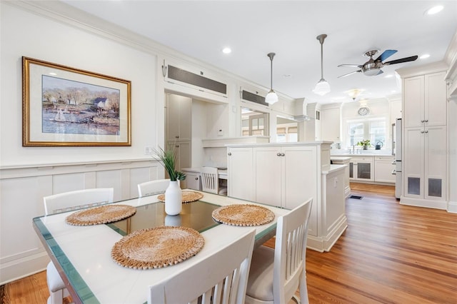 dining room with light wood finished floors, ornamental molding, recessed lighting, a decorative wall, and ceiling fan