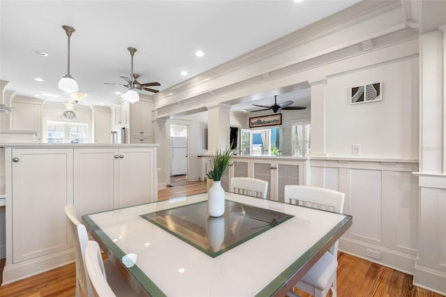 dining area featuring light wood-type flooring, a decorative wall, plenty of natural light, and ornate columns