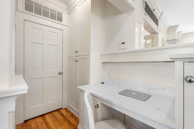 home office with light wood-type flooring, visible vents, and built in desk