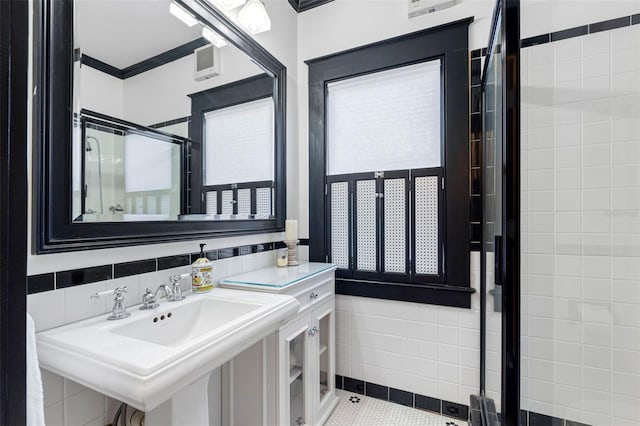 bathroom with a sink, tile walls, a stall shower, and ornamental molding