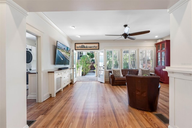 living area featuring ceiling fan, stacked washer / dryer, light wood-type flooring, and ornamental molding