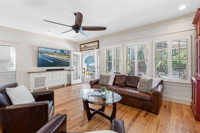 living area with a ceiling fan, light wood-style floors, baseboards, and ornamental molding