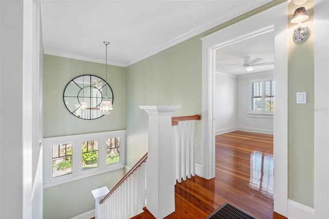 corridor with wood finished floors, baseboards, ornamental molding, an upstairs landing, and a chandelier