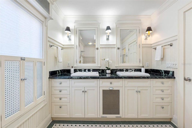 full bath with a sink, ornamental molding, double vanity, and a decorative wall