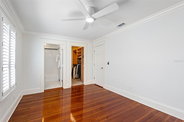 unfurnished bedroom with visible vents, a walk in closet, hardwood / wood-style flooring, a closet, and crown molding