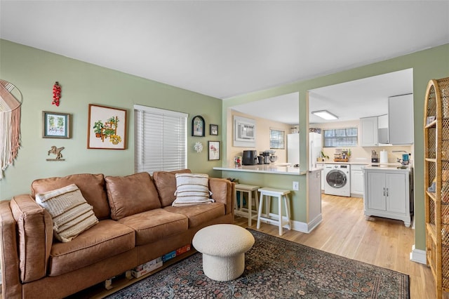 living area featuring washer / clothes dryer, baseboards, and light wood finished floors