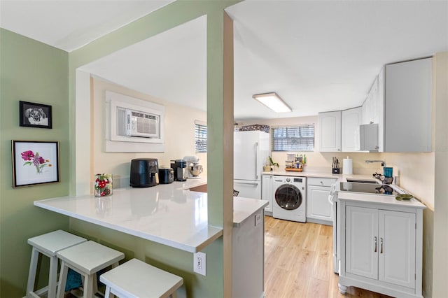 kitchen with washer / dryer, a peninsula, freestanding refrigerator, a kitchen breakfast bar, and light wood-type flooring